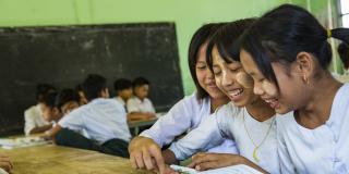 Three schoolgirls smile whilst sharing a textbook in the classroom at Kyakathone primary school, Mon state.