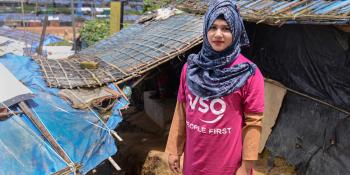 A volunteer in a VSO T-shirt stands in front of a temporary learning centre in the Cox's Bazar refugee camp