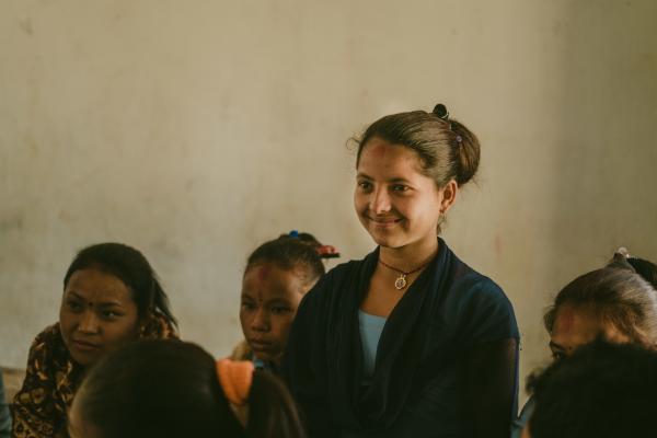 Nirmala smiles as she stands in the classroom, surrounded by her classmates who are sitting down