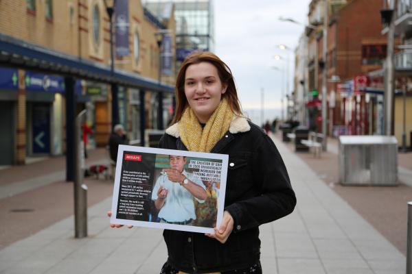 A young woman stands in a UK high street holding a poster which demonstrates the impact of campaigning for change
