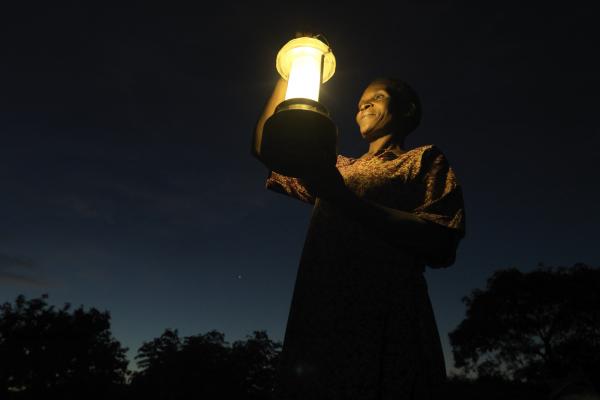 Solar Mama Dines is illuminated by a solar lantern she holds aloft as she stands outside in the night