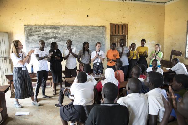 A group of ICS volunteers stands at the front of a school classroom, delivering a session on communication skills