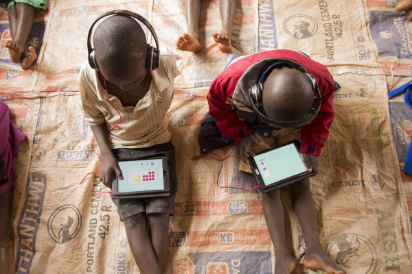 Two young schoolchildren sit on the floor at Mdzobwe Primary School and use their tablets to learn