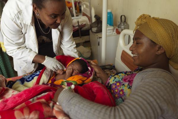 A mother smiles as she rests with her newborn baby, and a female doctor leans over to check on them