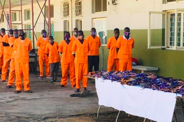 A group of prisoners in orange jumpsuits wearing masks