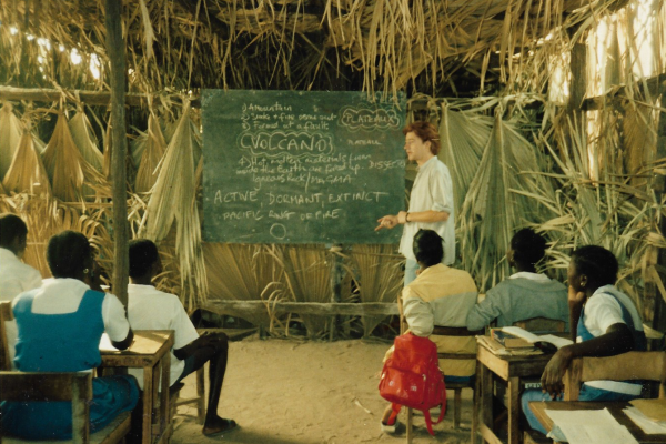 Man stood in the front of a rural classroom, giving a lesson to students in the Gambia