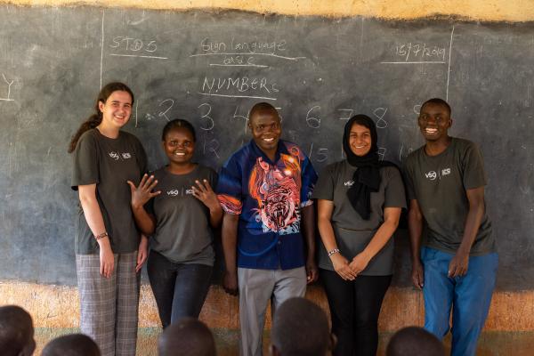 four volunteer standing at the front of a classroom, smiling at the camera