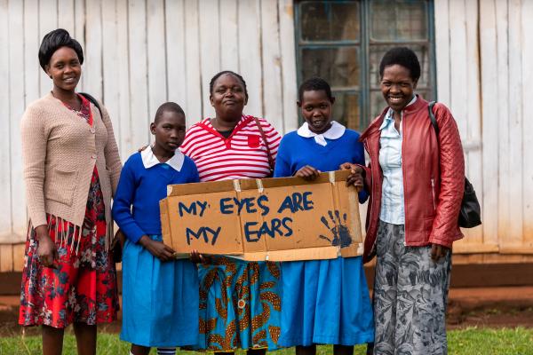 four people stood outside a building holding a sign that says 'my ears are my ears'