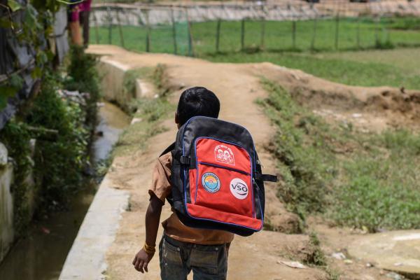 A Rohingya child runs with their new VSO backpack, filled with school supplies, so they can begin to learn the basics of education.