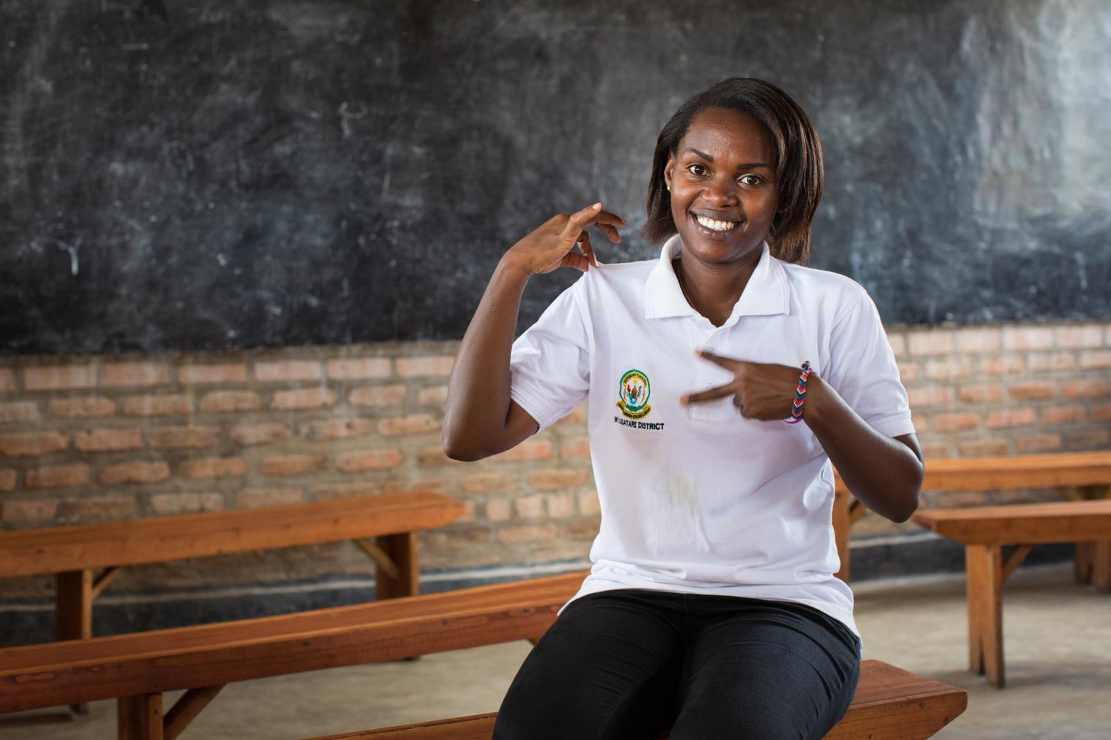 Volunteer Brown Niyonsaba smiles as she sits in front of a blackboard in the classrrom at Umutara School, signing 'VSO volunteer'