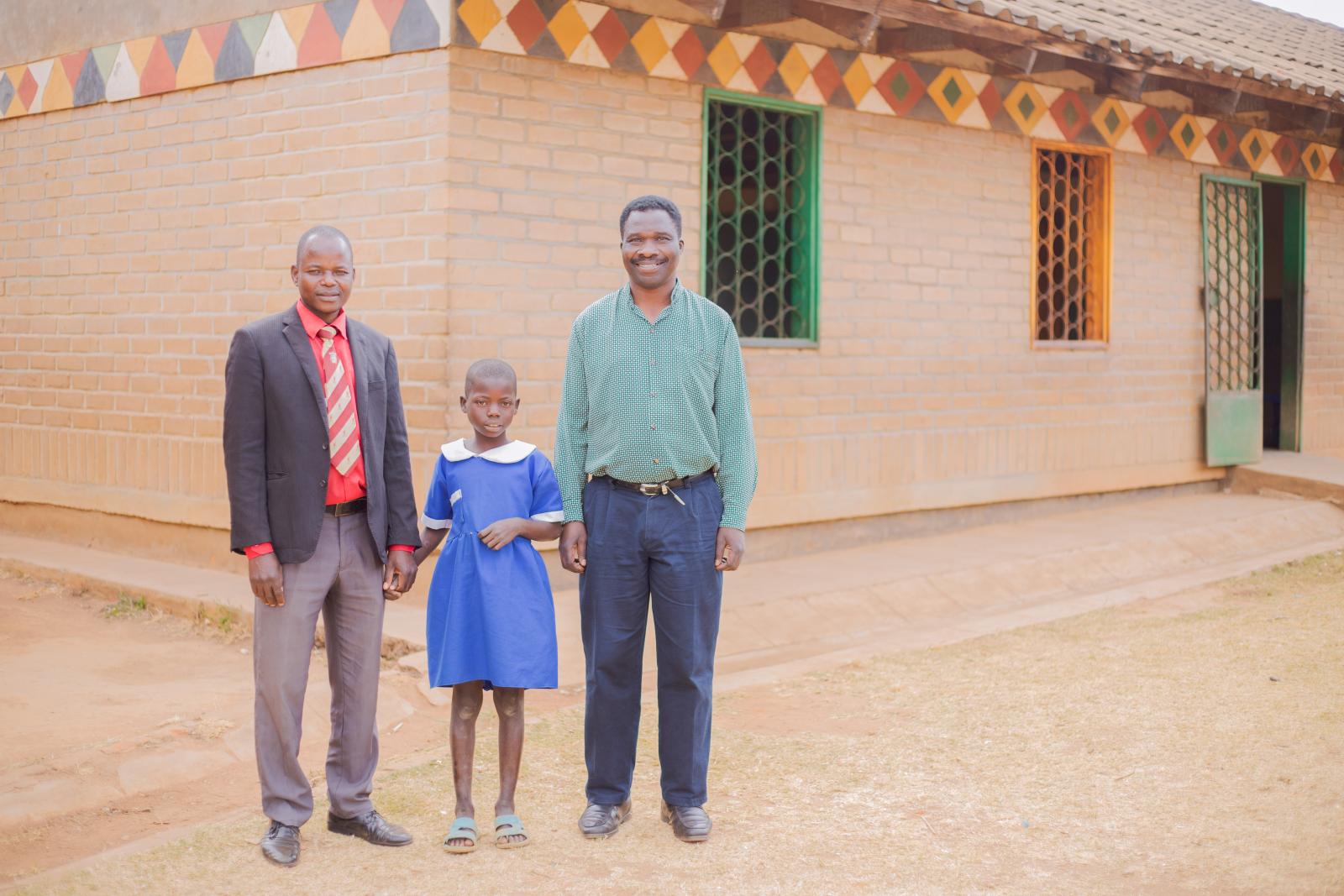 Peter, Alinafe and Theonas stand outside her classroom