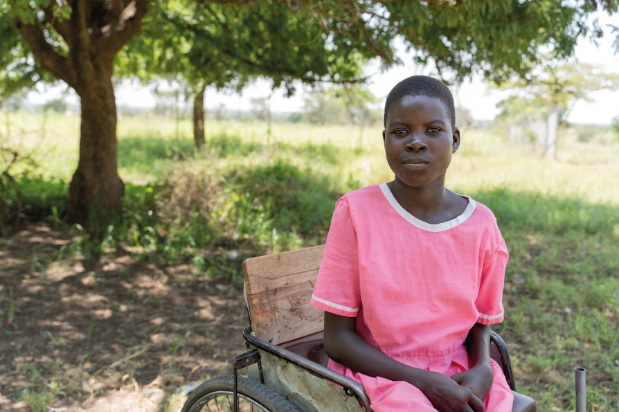 Nangiro sat on her wheelchair, outside, in a pink dress.