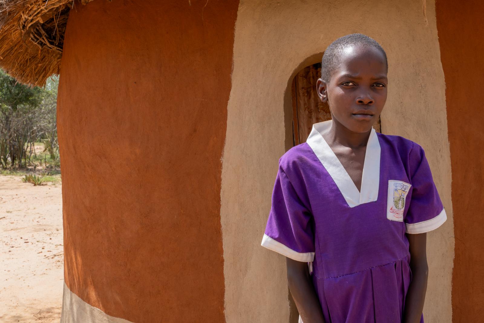 Young student, Nakiru, standing outside her home. 