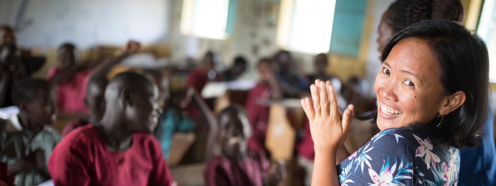 Volunteer Janice Ann Perez turns and smiles as she stands at the front of a full classroom in Karamoja, Uganda