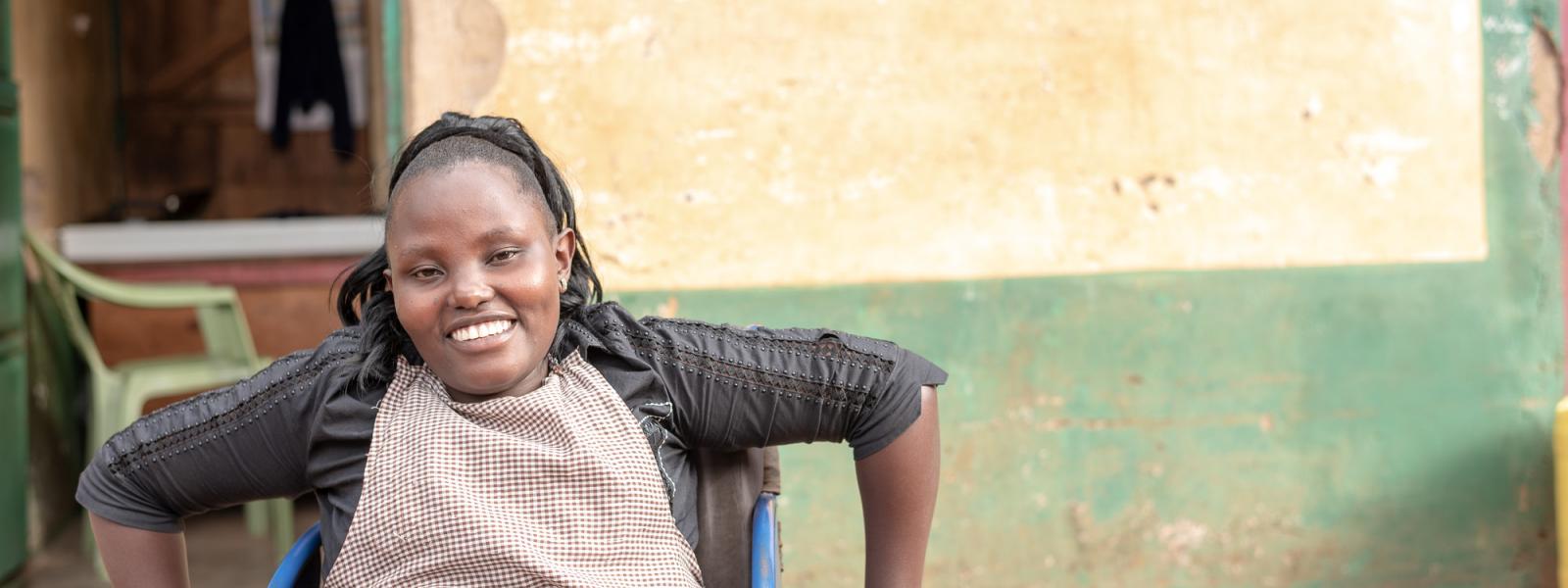 A young woman smiles as she poses in her wheelchair in front of a building