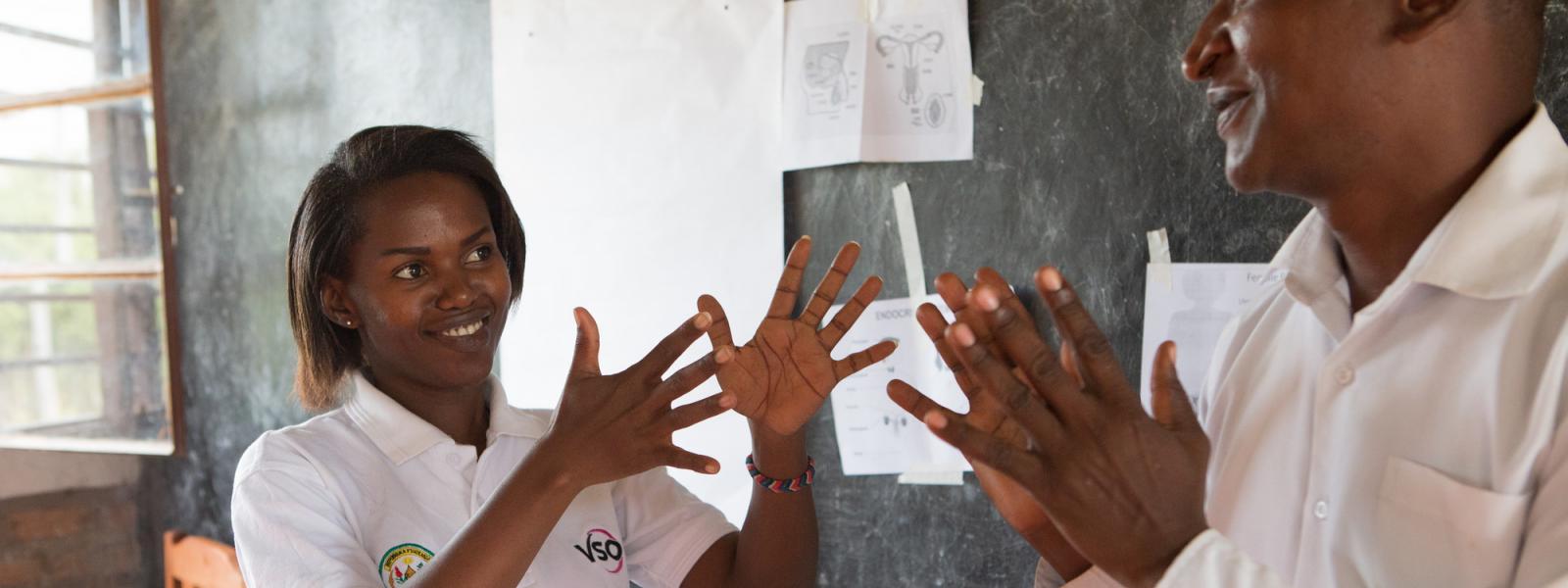 Volunteer Brown Niyonsaba signs with a fellow teacher in front of the blackboard, as part of a lesson on sexual and reproductive health