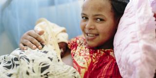 A smiling young mother lies in a hospital bed and holds her newborn baby on her chest