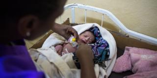 A midwife tends to a newborn baby who is wrapped in colourful blankets