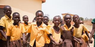 A group of primary schoolchildren hold hands and laugh as they play outside in the schoolyard.