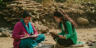 An older woman and a teenage girl sit outside on the ground in Nepal, studying
