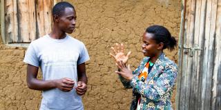 A young man and young woman stand outside, conversing in Rwandan Sign Language