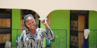 A woman punches the air and smiles in the street outside a row of buildings