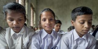 Two young girls and a young boy sit and read from their textbooks in a busy classroom
