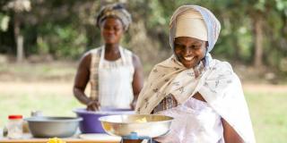 A woman smiles as she weighs ingredients for baking as part of an enterprise training group in Tutuka, Ashanti Region