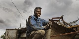 Arthur smiles as he sits atop some scrap metal in his welding yard