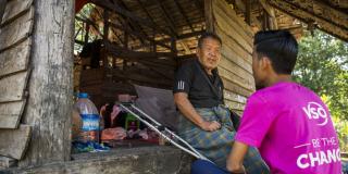 VSO national volunteer Kaung Khant speaks to a villager on the front porch of his house as part of his work identifying vulnerable residents to prepare for disaster.