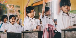 cambodia school girls stood at desks with their hands in the air