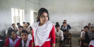 A schoolgirl stands up behind her desk to speak out against sexual harassment, whilst her classmates sit and listen