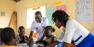 Volunteer Peter and teacher Jackline help some girls who are working together at a large table