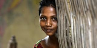 A young girl smiles slightly as she peers out from behind a wall in Parsa, Nepal