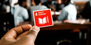 Close up of a hand holding a small red card with "4 - Quality Education" written on it
