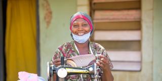 Smiling woman in mask at sewing machine.