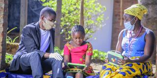 Child working on laptop with parents. Malawi.