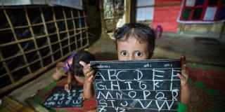 A Rohingya girl holding up her alphabet practice