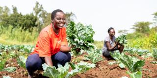 Two women in a field in Kenya smiling with their cabbages.