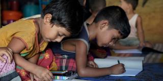 Two young Rohingya boys sit on the floor of a child-friendly centre in the Cox's Bazar camp, drawing with colouring pencils
