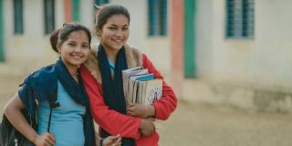 16-year-old Nirmala smiles with her friend, who is carrying a pile of schoolbooks.