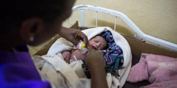 A midwife tends to a newborn baby who is wrapped in colourful blankets