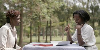 Volunteer Brown Niyonsaba sits across a table from a female health worker, teaching her Rwandan Sign Language