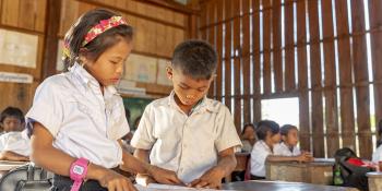 Two young schoolchildren stand at their desk and study together from a textbook