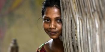A young girl smiles slightly as she peers out from behind a wall in Parsa, Nepal