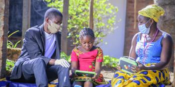 Child working on laptop with parents. Malawi.