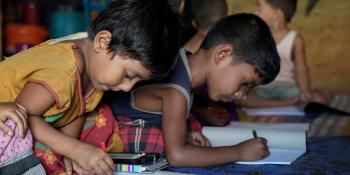 Rohingya children draw pictures in a home-based child-friendly centre in the Cox's Bazar camp, Bangladesh. Two young Rohingya boys sit on the floor of a child-friendly centre in the Cox's Bazar camp, drawing with colouring pencils