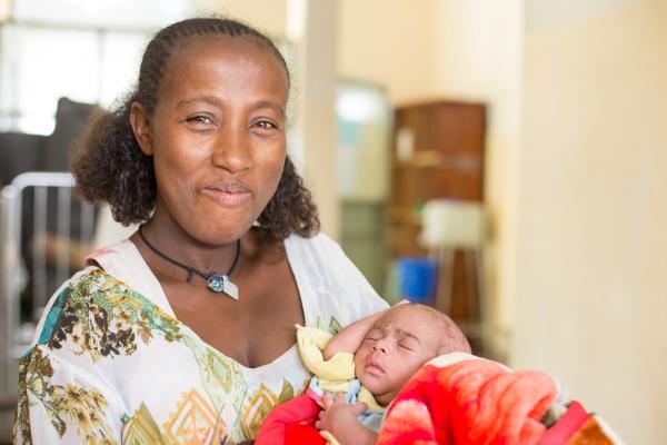 A smiling mother holds her one-month old baby in the NICU