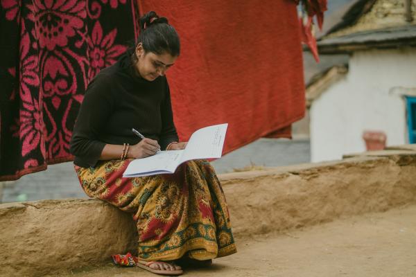 A woman sits on a low outdoor wall whilst writing in a log book