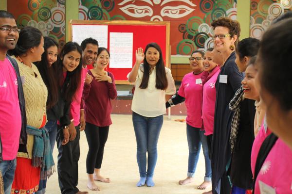 A woman raises her hand in the middle of a group of smiling community volunteers, at a theatre training workshop